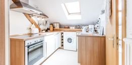 Helle Dachküche mit Holzdetails, modernen Geräten und Waschmaschine unter einem Dachfenster.