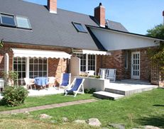 Backsteinhaus mit Terrasse, Sitzbereich und Sonnenschirmen, umgeben von grünem Garten.