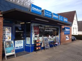 Fassade eines Autoteileladens mit blauer Beschilderung und Werbeplakaten vor dem Eingang.