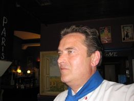 Ein Mann in einem Restaurant mit einem blauen Schal, im Hintergrund Gemälde und Beschilderung.