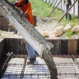 Worker pouring concrete into a rebar frame at a construction site.