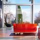 Bagno moderno con vasca rossa trasparente, vista su giardino e montagna attraverso ampie vetrate.