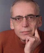 Eine Person mit Brille und orangenem Pullover schaut nachdenklich in die Kamera.