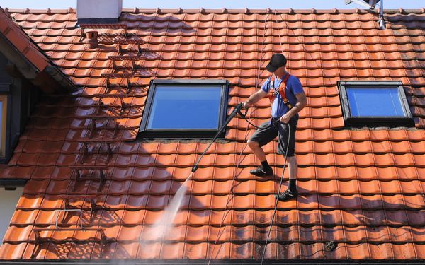 Ein Mitarbeiter eines Fachbetriebs für Dachreinigung, reinigt mit einem Hochdruckreiniger die Dachpfannen eines Einfamilienhauses.