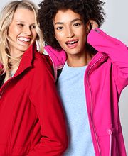 Zwei lächelnde Frauen in roten und pinken Jacken vor einem grauen Hintergrund.