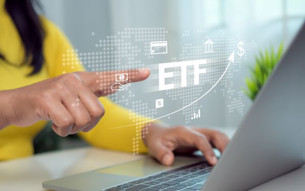 Geschäftsfrau zeigt auf ein Symbol ETF, welches vor ihrem Laptop erscheint.