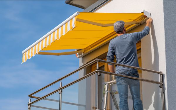 Ein Monteur steht auf einer Leiter und kontrolliert den Motor der montierten Markise.
