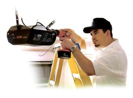 Man on ladder using drill to install garage door opener.