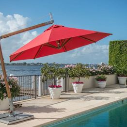 Sonnenschirm am Pool mit Blick auf das Wasser, umgeben von Pflanzen in weißen Töpfen.