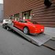 Red sports car being towed on a flatbed truck in an urban setting.