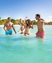 Cuatro personas disfrutando en el mar cerca de una playa con palmeras y cielo despejado.