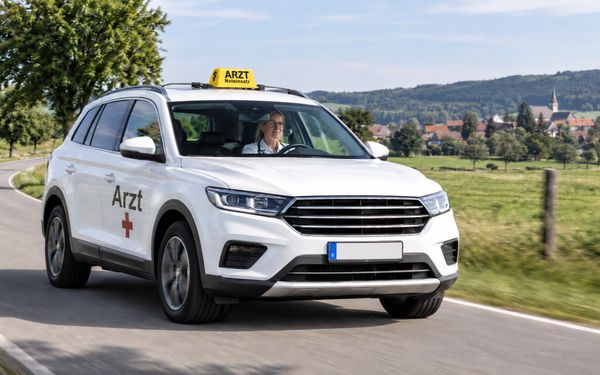 Weißer Arzt-SUV mit gelbem „ARZT Noteinsatz“-Dachschild auf einer Landstraße in ländlicher Umgebung.
