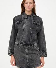 Mujer con chaqueta y falda de mezclilla negra, posa sobre fondo blanco.