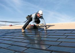 Worker installing solar panels on a rooftop under a blue sky.