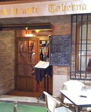 Entrada de una taberna con mesas al aire libre, menú en pizarra y decoración rústica.