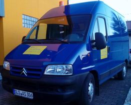 Blaue Citroën-Transporter mit gelben Aufklebern, parkt vor einem orangefarbenen Gebäude.