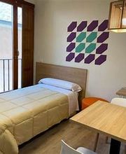 Habitación con cama individual, mesa, silla, lámpara y decorado geométrico en la pared.