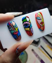 Uñas postizas decoradas con coloridos diseños cubistas sostenidas por una mano.