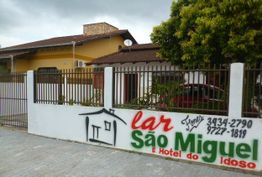 Fachada de um edifício com placa "Lar São Miguel e Hotel do Idoso" ao lado de um portão.