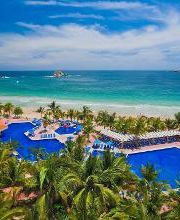 Piscina grande junto a una playa tropical con palmeras y cielo despejado.