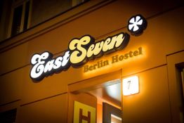 Leuchtschild mit "EastSeven Berlin Hostel" an einem Gebäude bei Nacht im warmen Licht.