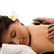 Woman receiving a hot stone massage, flower in hair, eyes closed, relaxing on a towel.