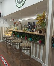 Bar con taburetes, estanterías con botellas y una planta decorativa. Señal "espere su turno".