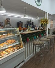 Cafetería acogedora con mostrador de pasteles y barra con taburetes. Decoración luminosa.