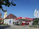 Esso-Tankstelle neben einem Gebäude mit Kirchturm im Hintergrund an einem sonnigen Tag.