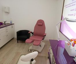 Sala de estética con silla reclinable rosa, muebles y lámpara, tonos morados y blancos.