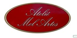 Placa oval vermelha com texto "Ateliê Mel Artes" em letras cursivas brancas.