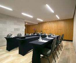Sala de conferência vazia com mesas retangulares cobertas por toalhas pretas e cadeiras alinhadas.