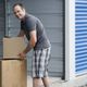 Man in plaid shorts lifting boxes outside a storage unit.