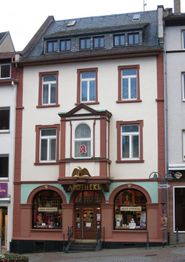 Fassade einer Apotheke in einem historischen Gebäude mit drei Stockwerken und roten Akzenten.