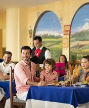 Grupo de personas sonriendo en restaurante con un mural colorido de fondo.