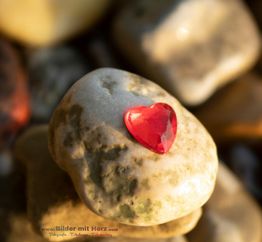 Roter Herzstein auf einem großen Kiesel vor unscharfem Hintergrund.