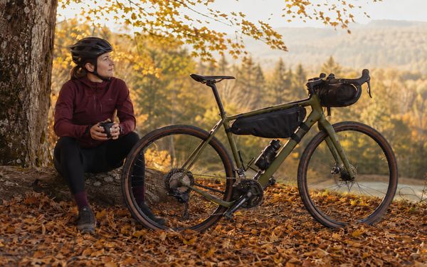 Frau macht im Herbst neben einem Gravel Bike auf ihrer Bikepacking-Tour eine Pause und genießt die Aussicht.