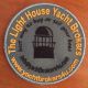 Rond embleem met oranje tekst: "The Light House Yacht Brokers" en een afbeelding van een vuurtoren.