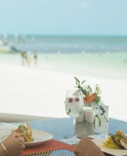 Dos personas almuerzan frente al mar en una terraza, con bebidas y platos de comida.