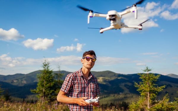 Mann mit Sonnenbrille fliegt eine Drohne in den Bergen und muss dabei auf die neuen Vorschriften für Drohnenfotografie achten.