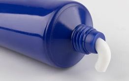 Blue tube with white cream oozing from the open nozzle on a light background.