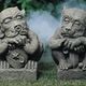 Zwei groteske Gargoyle-Statuen auf Gras, umgeben von leichtem Nebel.