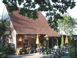Gemütliches Café mit rotem Dach, umgeben von Bäumen und Tischen mit gelben Sonnenschirmen.