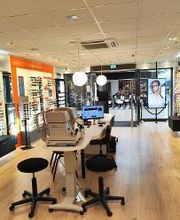 Optiekwinkel met brilrekken, een tafel en stoelen in een moderne en lichte ruimte.