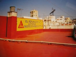 Azotea roja con anuncio amarillo de reparación de goteras y número de teléfono. Edificios al fondo.