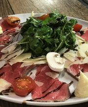 Carpaccio mit Rucola, Kirschtomaten, Parmesan, Pilzen und Cremetupfen auf einem Teller.