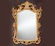 Ornate gold-framed mirror with intricate details, set against a dark background.
