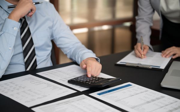 Zwei Mitarbeiter eines Unternehmens checken die Jahresendzahlen des Unternehmens an einem Bürotisch.