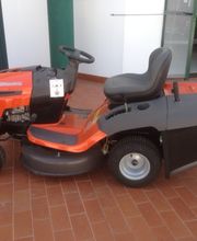 Trattorino rasaerba arancione e nero su pavimento di mattoni vicino a un garage.