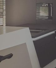 Moderne Küche mit grauem Möbel-Design und einer weißen Arbeitsplatte, neben einem Fenster.